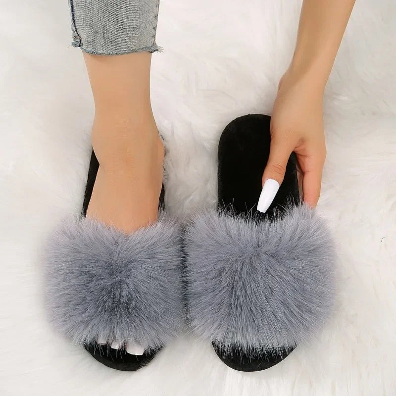Gray fuzzy flat slide slippers with plush fur strap worn by person sitting on white fuzzy rug